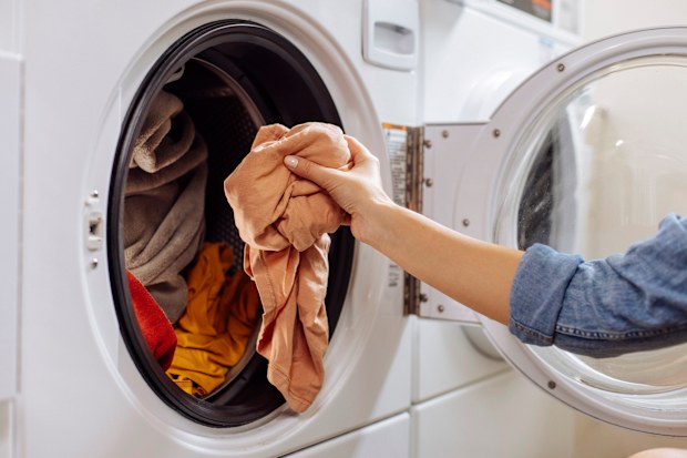 Woman putting dirty clothes and laundry into washing machine
