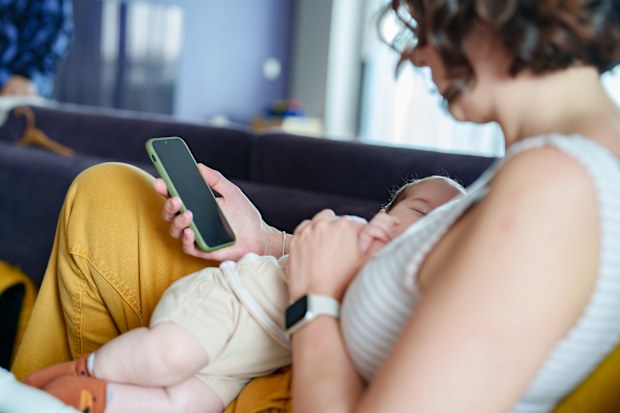 Mother breastfeeding her baby and using mobile phone at home