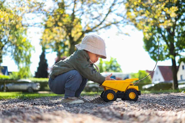 Toddler boy playing on the playground outside with his plastic car