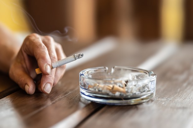 Stock image of a woman smoking and tapping cigarette ash into an ashtray.