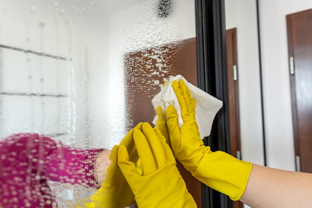 Woman’s hand in a glove with a spray washes and cleans the glass in the wardrobe