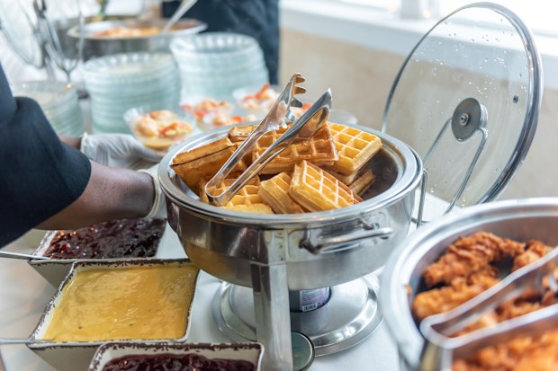 A closeup shot of a buffet table with waffles and various types of toppings being served