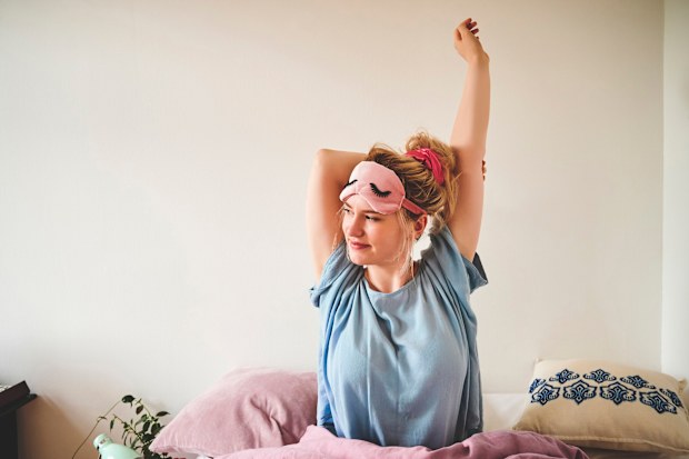 woman sitting in bed and stretching after waking up in the morning