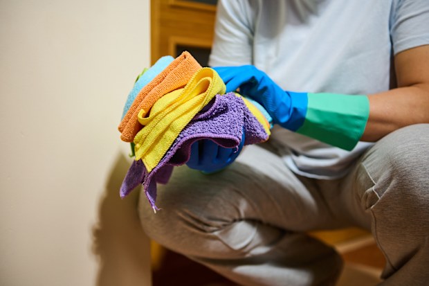 Woman cleaning her home, wearing blue rubber gloves and holding colourful microfibre cloths for household chores and tidying and sanitation.
