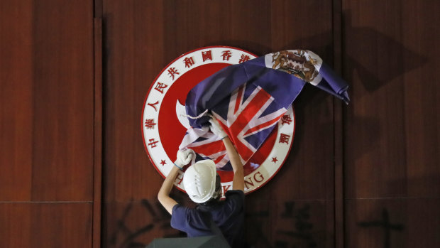 A protester covers the Hong Kong emblem with the Hong Kong colonial flag in the Legislative Council chambers during protests on Monday.