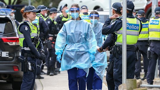 Medical staff wearing PPE holding material about to walk into the Flemington public housing flats on Sunday.