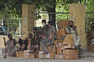 Indians labourers sit on boxes of medicines and wait for markets to open early morning in Jammu, India on Wednesday.