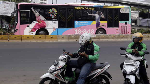 Motorcycle taxi drivers wait for customers as a bus with Asian Games promotional stickers drives past in Jakarta.