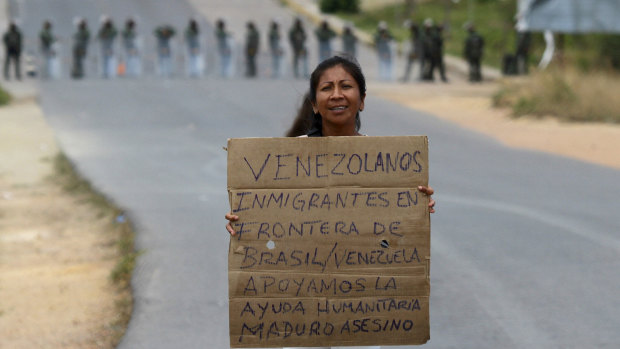 A Venezuelan holds a sign that reads in Spanish:  Venezuelan migrants at the border between Brazil-Venezuela, we support the humanitarian aid. Maduro assassin. 
