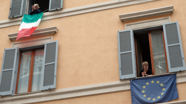 Italian and European Union flags hang from windows in a  Rome street. 