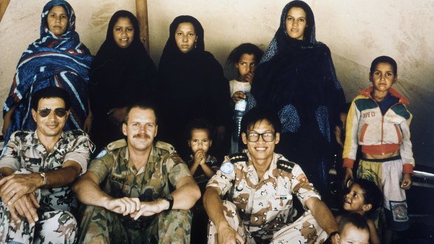 Group portrait of United Nations Military Observers (UNMOs) from MINURSO (United Nations Mission for the Referendum in Western Sahara) with Polisario wives and local children. Major Carey is seated second from left.