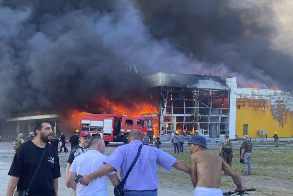 People watch as smoke pours from a crowded shopping mall in Kremenchuk after a Russian missile strike.