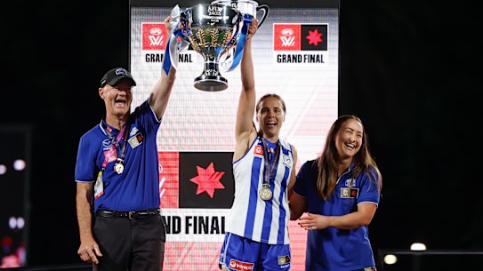 Darren Crocker, Senior Coach of the Kangaroos, Jasmine Garner of the Kangaroos and Nicole Bresnehan of the Kangaroos hold the Premiership Cup aloft.