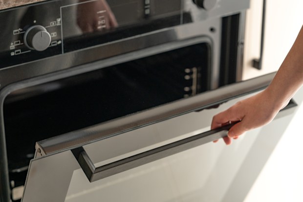 A person’s hand open a modern built-in oven in the kitchen. 