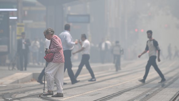 Pedestrians cross a hazy George Street as smoke haze blankets Sydney on Tuesday.