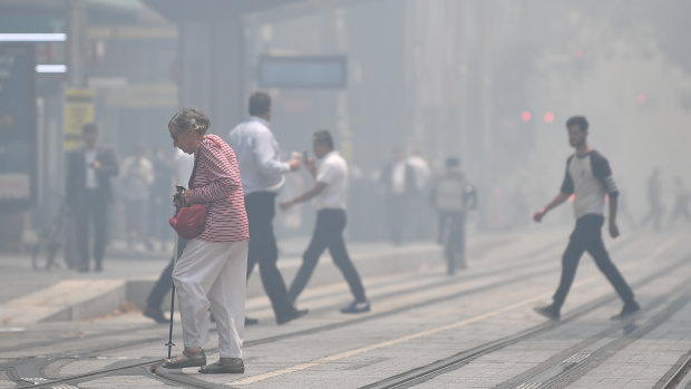 Pedestrians cross a hazy George Street as smoke haze blankets Sydney on Tuesday.