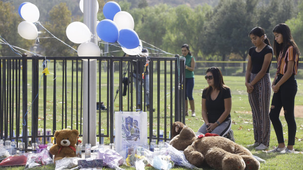 Parent Mirna Herrera kneels with her daughters Liliana, 15, and Alexandra, 16 at a memorial for the Saugus High School victims.