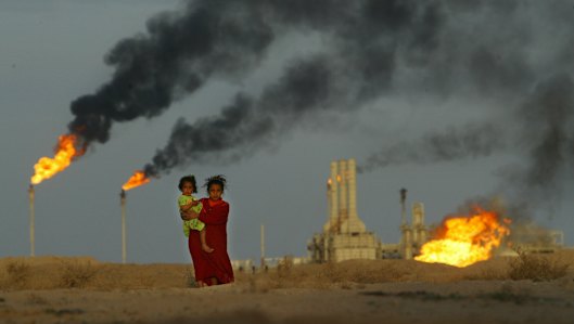 A young girl and her baby sister emerge from the heat and smoke from a petrochemical plant near their family farm, just north of the Iraq-Kuwait border. 