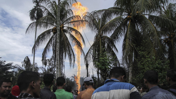 Curious onlookers watch as an oil well burns after it caught fire in eastern Aceh, Indonesia.