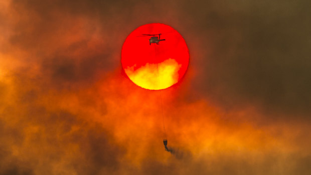 A firefighting helicopter makes a water drop as the sun sets over a ridge burning near Redding, California. 