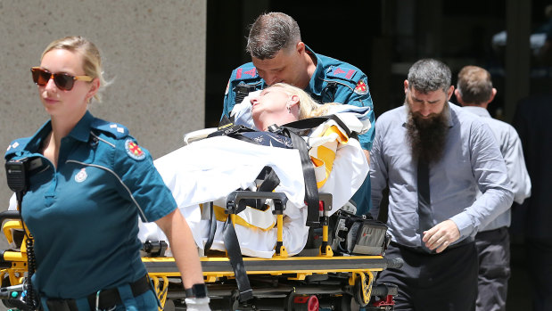 Julie Connor is taken by paramedics from the Federal Court in Brisbane, after having a medical episode, as her husband Peter (right) follows.