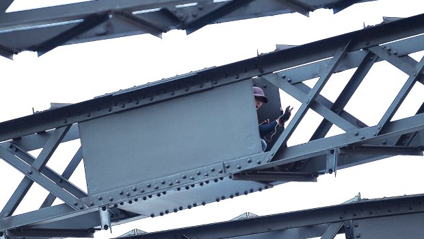 The man sits in a box in the framework of the Sydney Harbour Bridge as police negotiate with him.