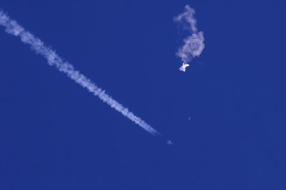 The remnants of the large balloon drift above the Atlantic Ocean, with a US fighter jet and its contrail seen below it.