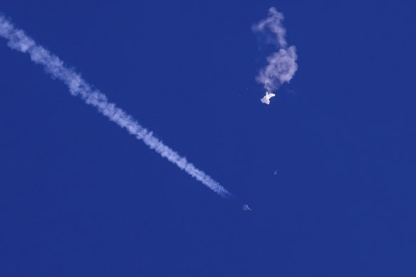 The remnants of a large balloon drift above the Atlantic Ocean, with a fighter jet and its contrail seen below it.