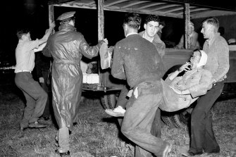 Gamely smoking a cigarette, this battered victim of the Hindenburg dirigible air catastrophe is carried to an ambulance waiting on the field at Lakehurst. 