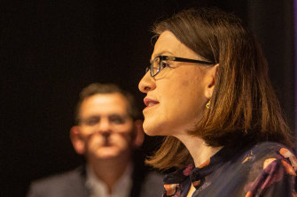 Daniel Andrews watches his then health minister Jenny Mikakos at the podium.