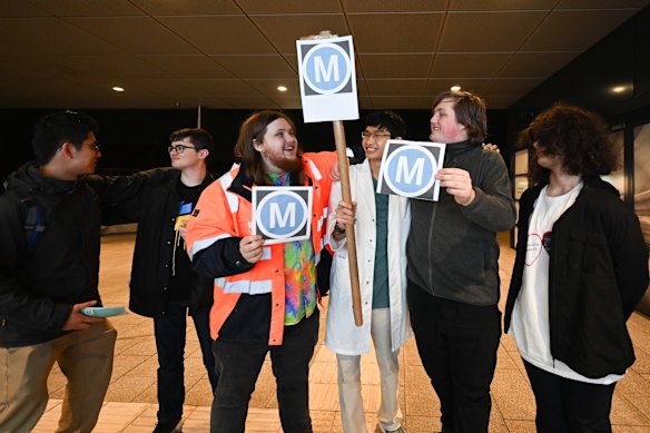 Thomas Marynissen, Wesley Fung, and Logan Newboult-Kosztyo, carrying Metro signs, wait for the first Metro train on the M1 line at Sydenham station.