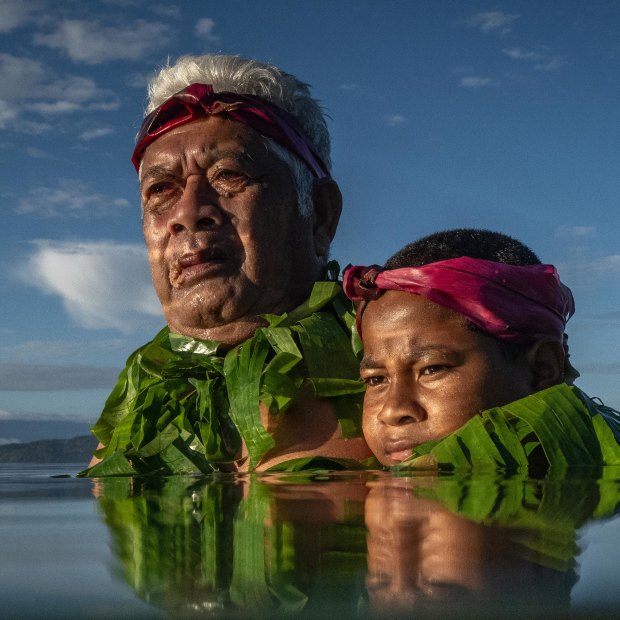 Kioa island resident Lotomau Fiafia and his grandson John. Lotomau was born on the island in 1952 and has seen erosion of the shoreline in the past decades. He stands in the water roughly where the shoreline used to be when he was young.