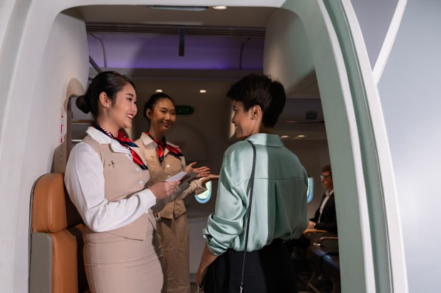 Female flight attendants in suit uniform standing at airplane entrance and checking woman passenger boarding pass for flight information