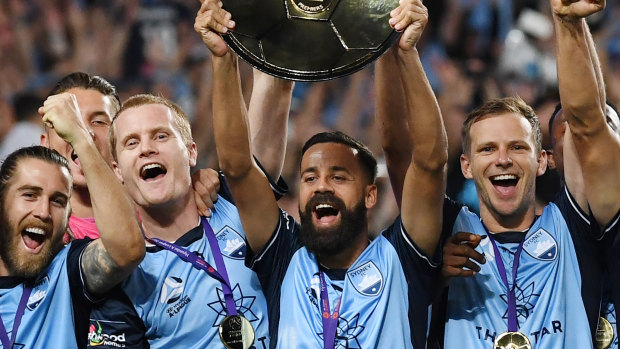 Sydney FC captain Alex Brosque lifts the A-League premiers plate with Alex Wilkinson to his right.