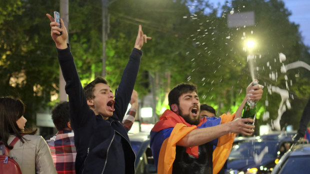 A man covered with a national flag waves an opened bottle of a sparkling wine celebrating Armenian Prime Minister's Serzh Sargsyan's resignation in Republic Square in Yerevan.
