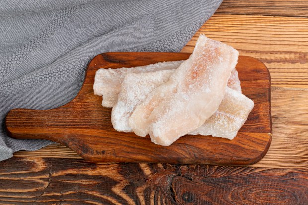 Frozen Fish on Wooden Cutting Board, White Cod Fillet, Iced Hake Filet, Frozen Pollock Meat on Rustic Wood Background Top View