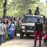 Security forces drive past a crowd of people gathered outside the Lhubiriha Secondary School following an attack on the school near the border with Congo, in Mpondwe, Uganda.