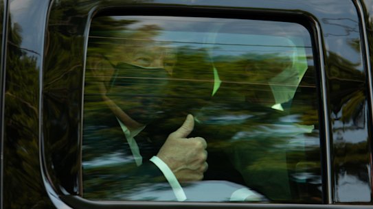 President Donald Trump wears a face mask while giving supporters a thumbs up from his motorcade.