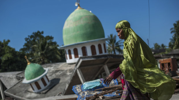 A Muslim woman walks past a mosque that collapsed after the earthquake in Gangga, Lombok Island.