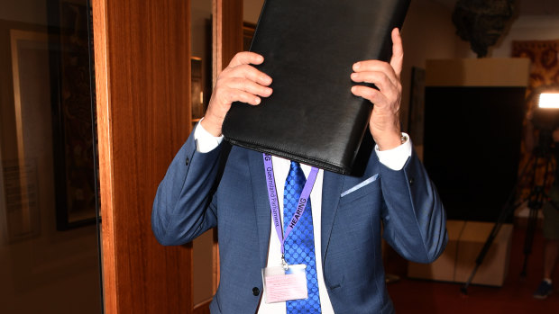 Mr Miller covers his face as he arrives for the parliamentary inquiry hearing.