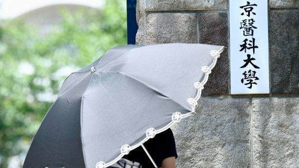 A woman walks past the gate of Tokyo Medical University. The plate reads: "Tokyo Medical University."