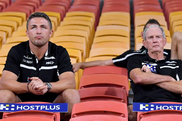 Sam Burgess (left) and Rabbitohs coach Wayne Bennett sitting in the empty grandstands during the round two NRL match between the Brisbane Broncos and South Sydney Rabbitohs at Suncorp Stadium in March.