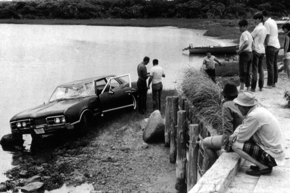 Spectators look on as police work near the car driven by Sen. Edward Kennedy which plunged off a bridge into an island pond on Chappaquiddick Island, July 1969.
