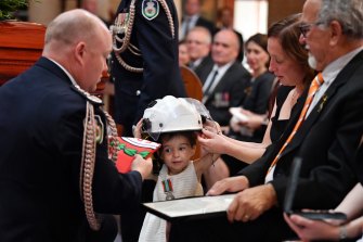 Charlotte O'Dwyer, the young daughter of RFS volunteer Andrew O'Dwyer, with Andrew's wife Melissa, receiving her father's helmet after being presented with his service medal by RFS Commissioner Shane Fitzsimmons.
