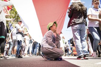A child takes shade under a giant flag as the crowd gathers on the steps of Parliament House.