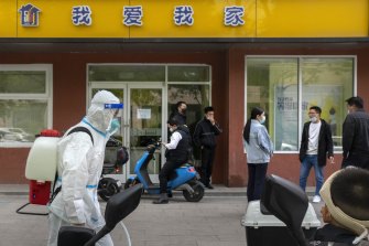 A worker wearing a protective suit and carrying a tank of disinfectant walks along a street in Beijing.