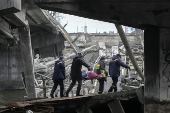 Ukrainian rescue workers carry an elderly woman under a destroyed bridge in Irpin, close to Kyiv, Ukraine, on Friday