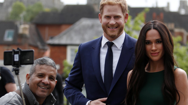 A tourist takes a selfie with the waxwork figures of Prince Harry and Meghan Markle against a backdrop of Windsor Castle.