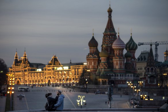 A couple enjoy warm weather on a bridge with St. Basil’s Cathedral, right, and an almost empty Red Square after sunset in Moscow, Russia.