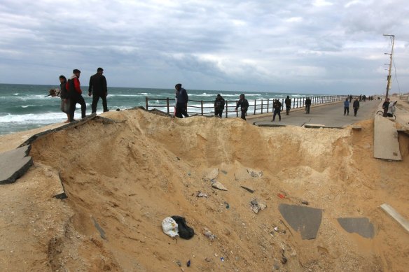 Displaced Palestinians pass a crater on the coastal road after fleeing the Al Shifa hospital area.